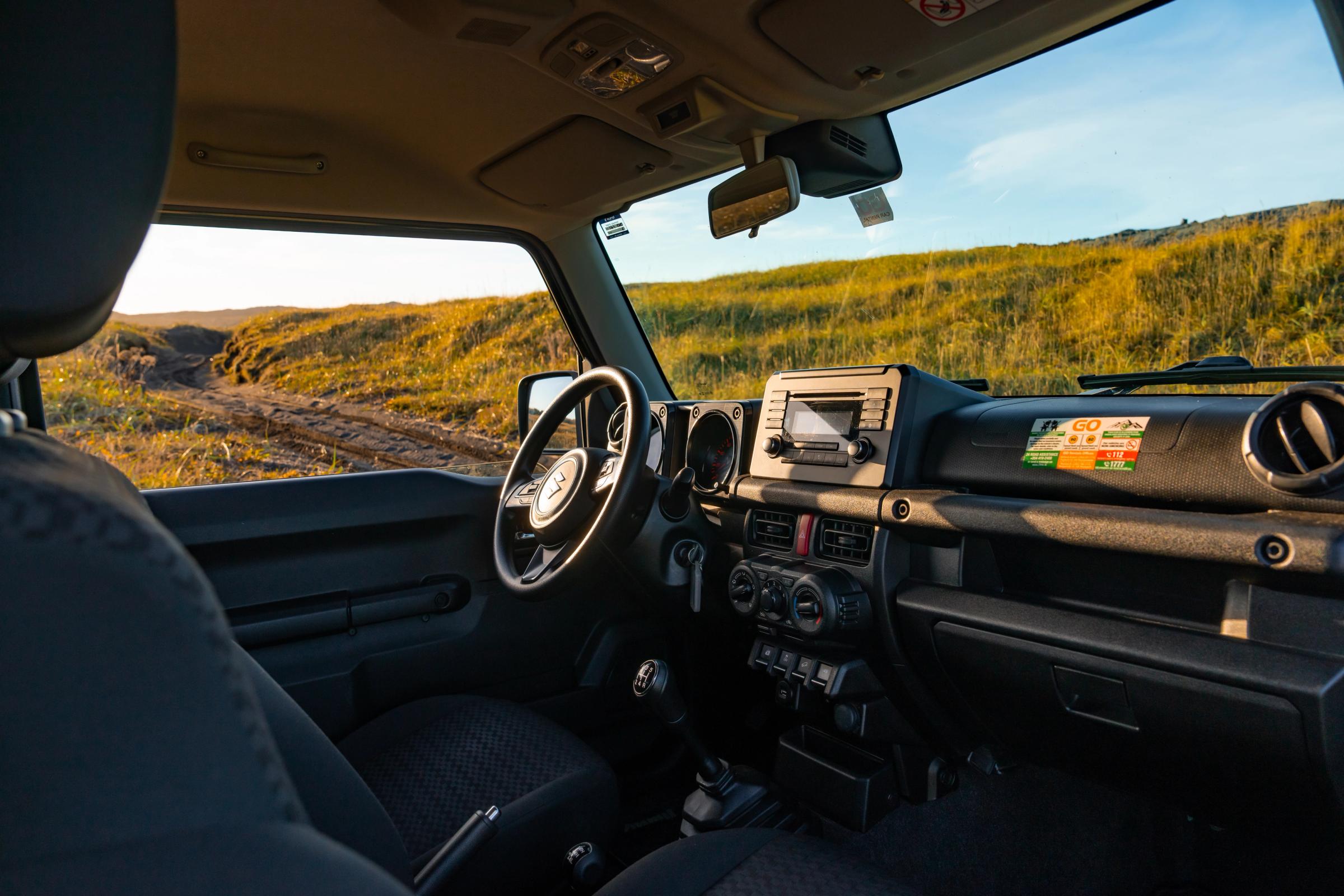 Armaturenbrett eines Suzuki Jimny mit Schaltgetriebe, Lenkrad und Radio, vom Rücksitz aus gesehen