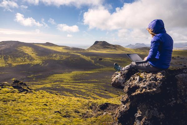 a person is sitting on a rock using a laptop computer .
