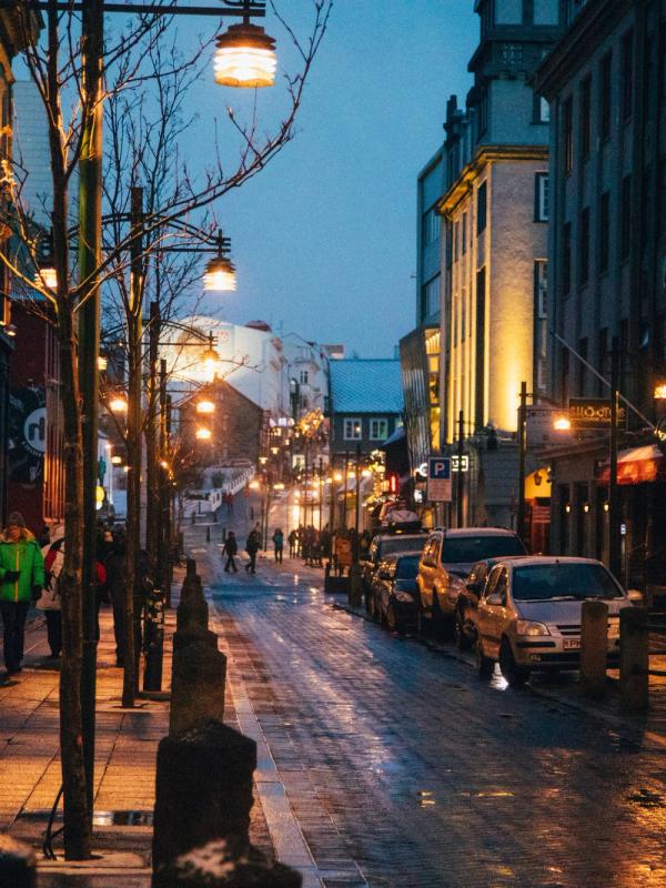 Reykjavik Iceland a city street at night with cars parked on the side of it and people walking down it .Reykjavik rainy night downtown in Iceland