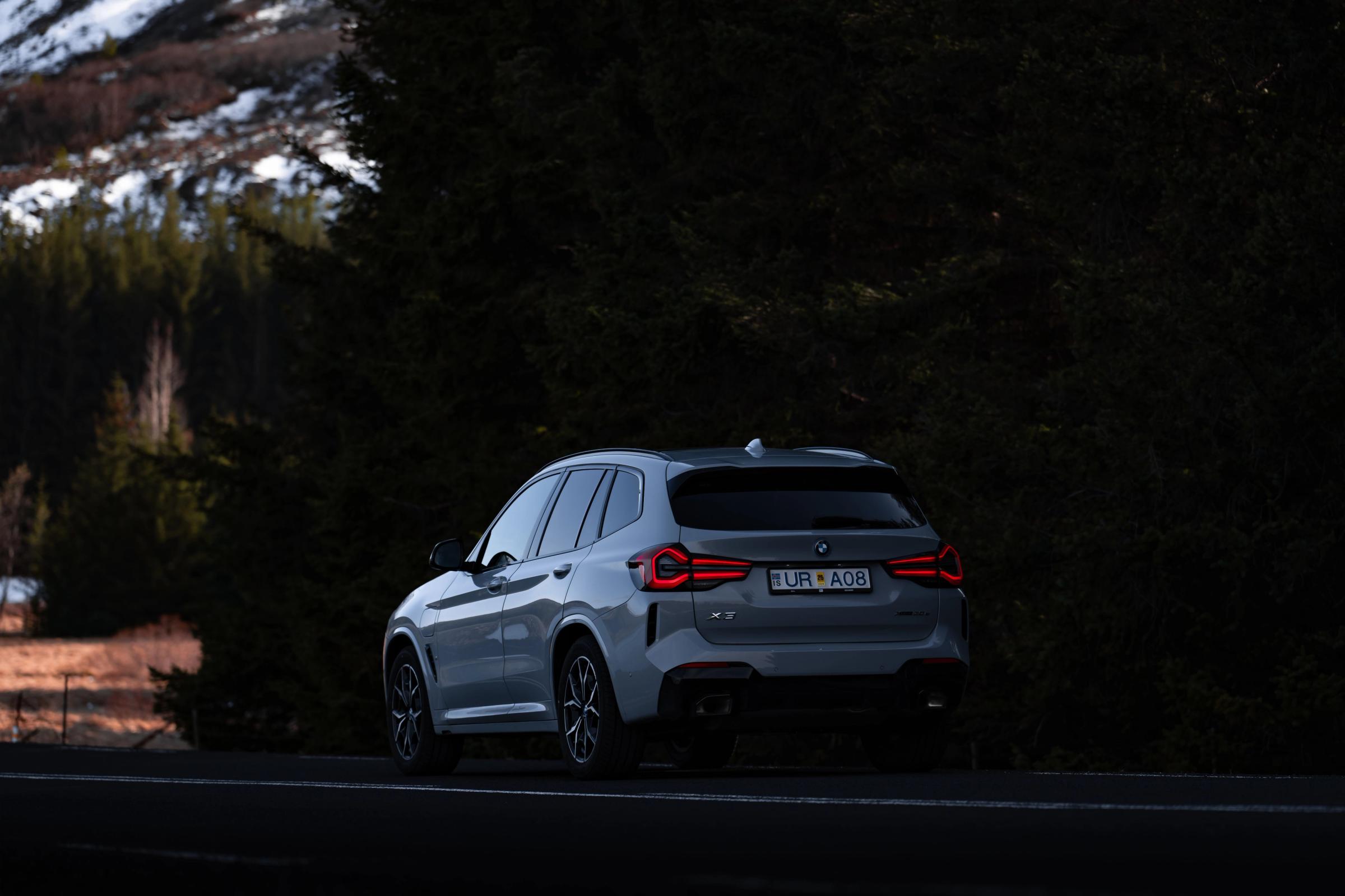 Vue arrière d’un BMW X3 4x4 de location en Islande, garé sur une route en bordure de forêt