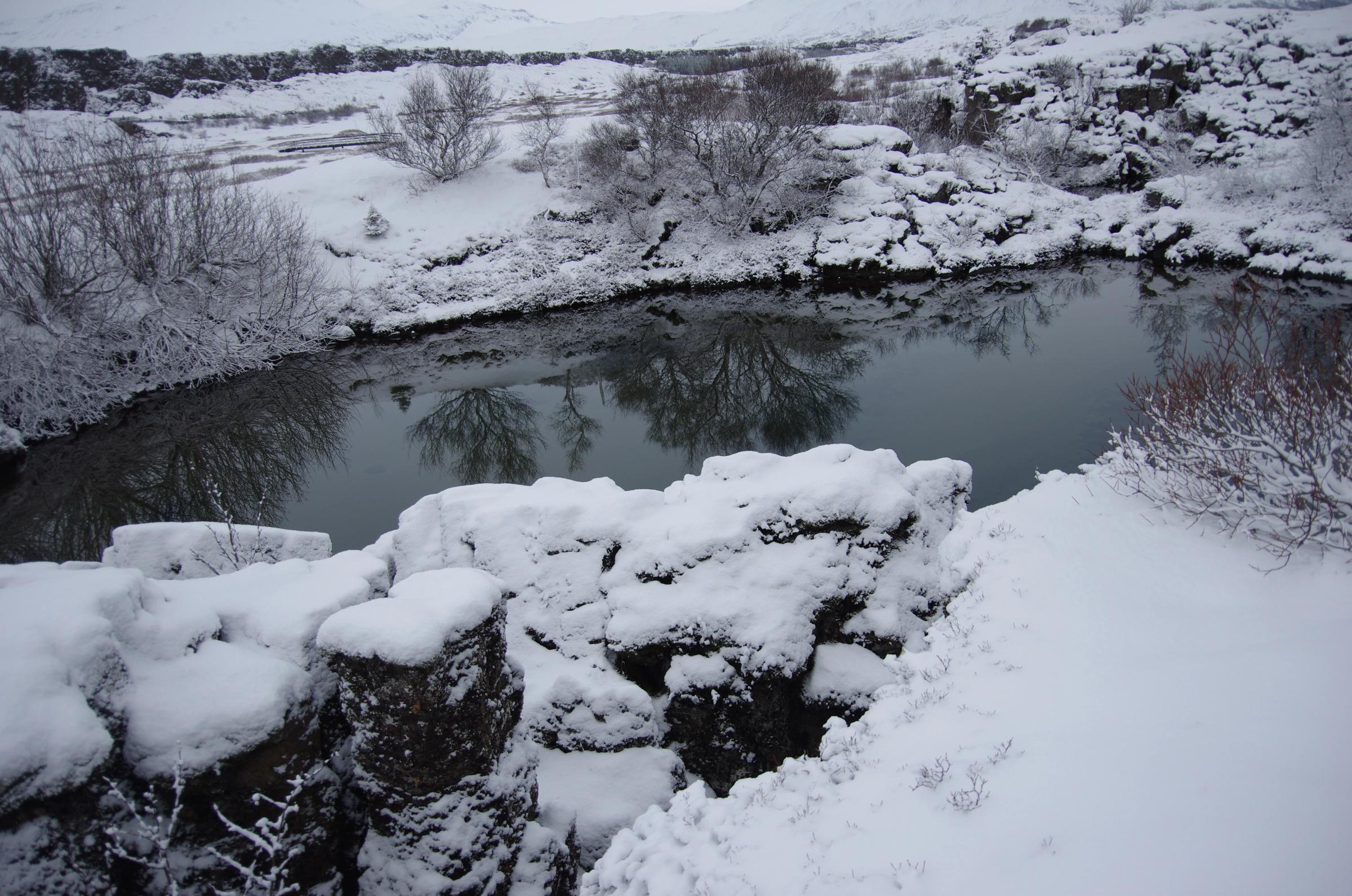 un río nevado rodeado de rocas y árboles cubiertos de nieve .