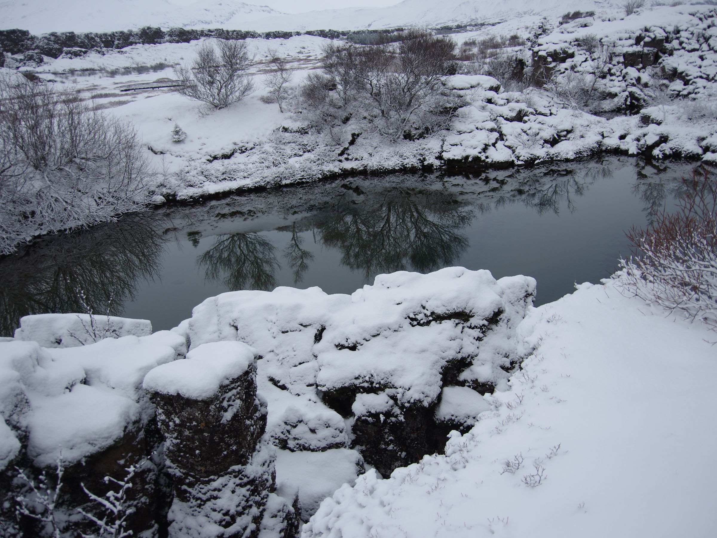un río nevado rodeado de rocas y árboles cubiertos de nieve .