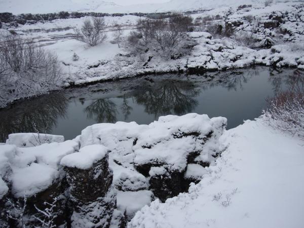 un río nevado rodeado de rocas y árboles cubiertos de nieve .