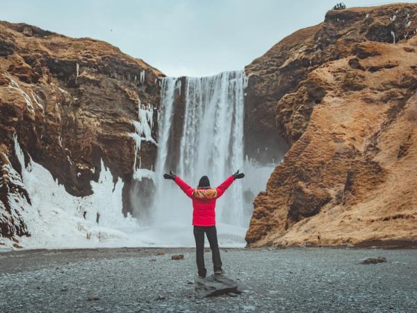 a person is standing in front of a waterfall with their arms outstretched .