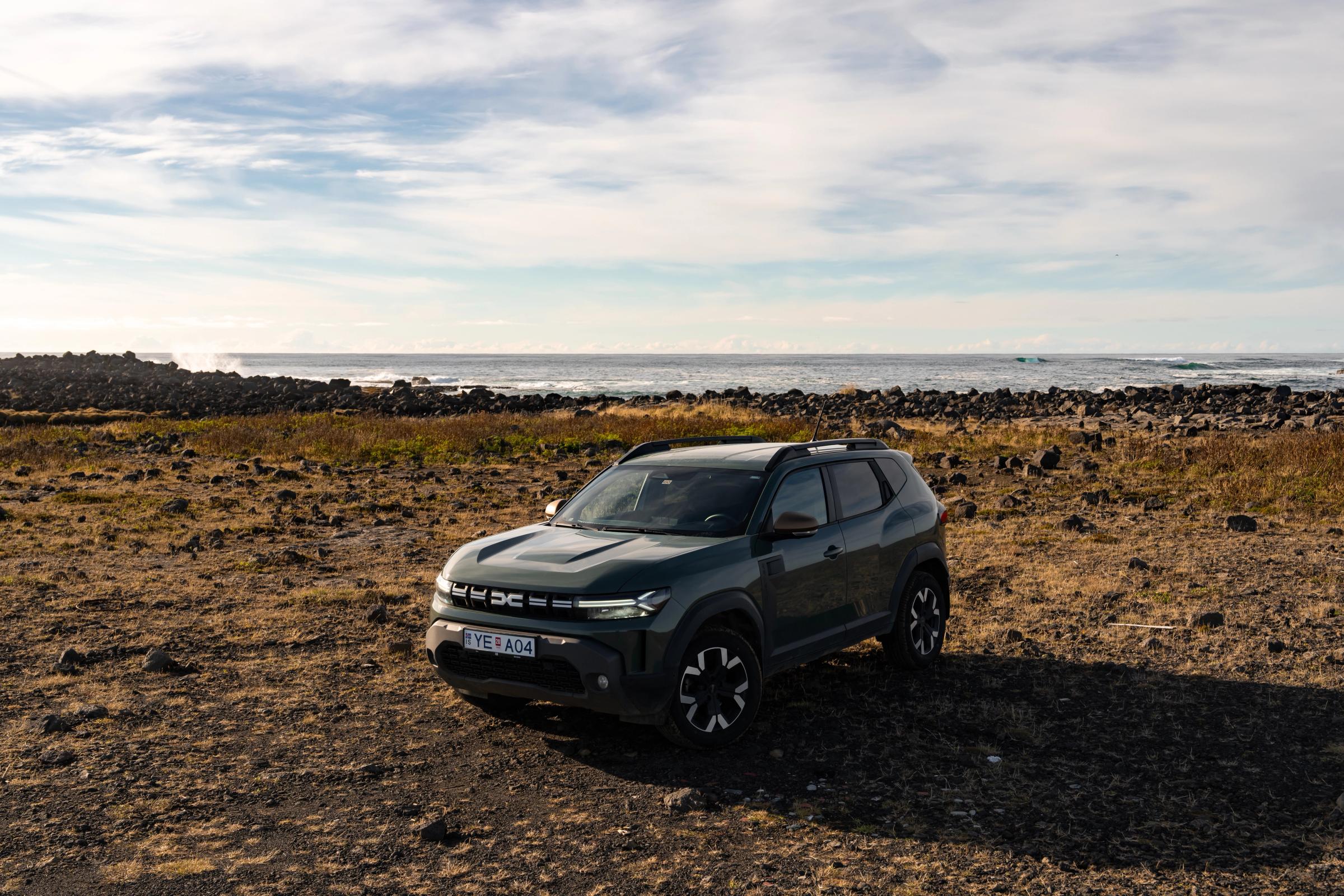 Vista dianteira a três quartos de um Dacia Duster estacionado num terreno rochoso aberto junto à costa