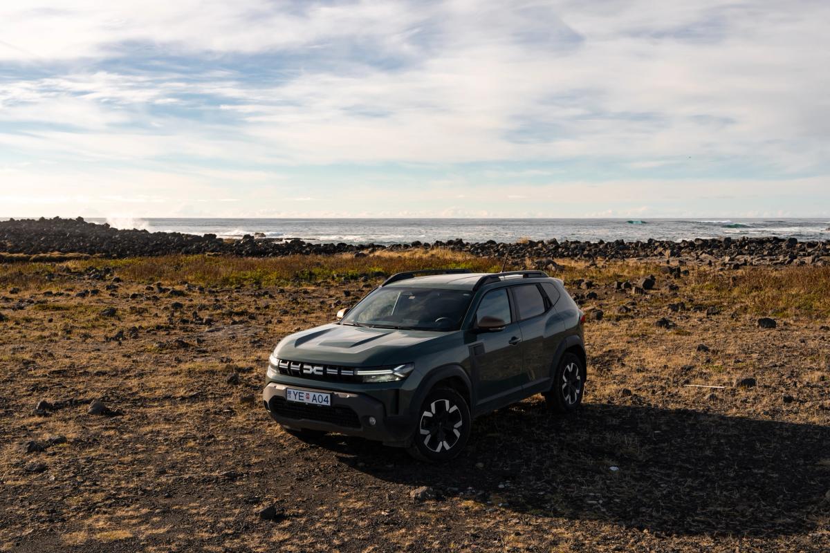 Vista dianteira a três quartos de um Dacia Duster estacionado num terreno rochoso aberto junto à costa
