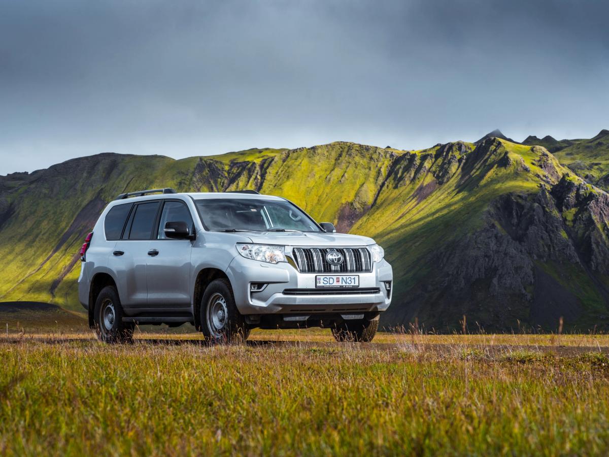 Land Cruiser Highland View Toyota Land Cruiser in schräger Frontansicht, auf einer Wiese unterhalb eines moosbewachsenen Bergrückens geparkt