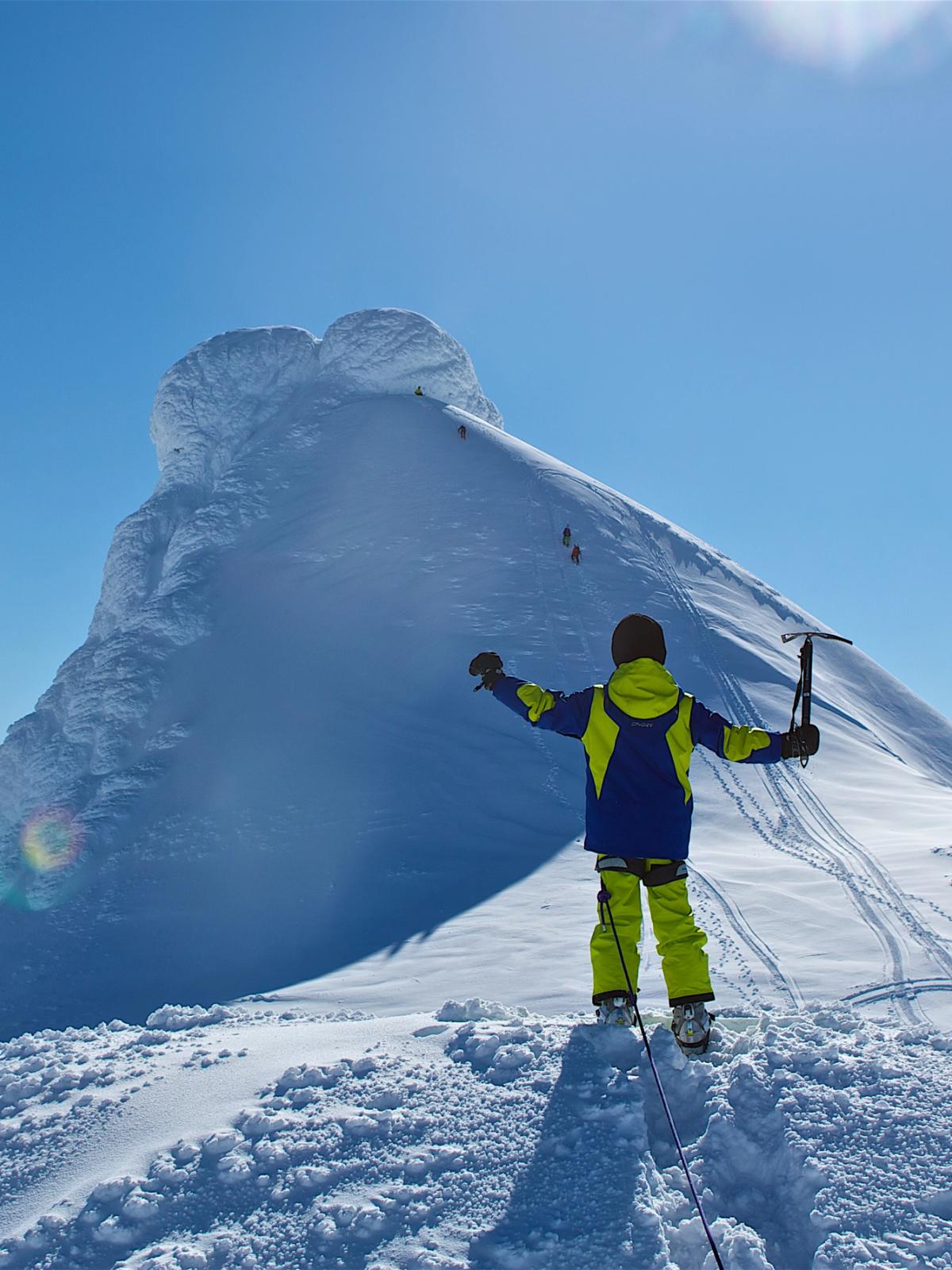 a person dress in snow clothes is in front of a snow covered mountain peak