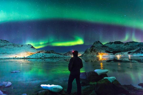 Northern Lights during winter, Iceland Exceptional view of a starry sky and aurora borealis in a winter landscape with snow-capped mountains. In the foreground a man alone admiring this spectacle