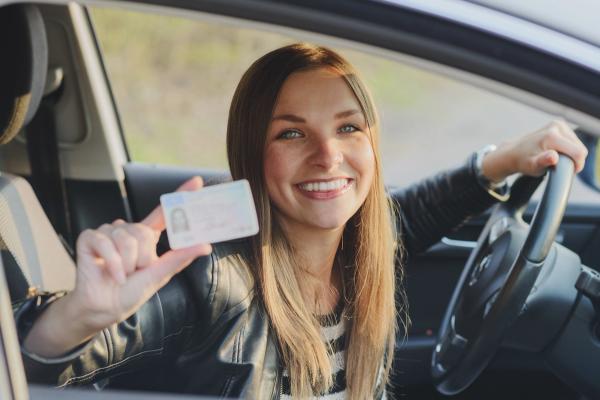 A smiling woman in a car holds up her driver's license.