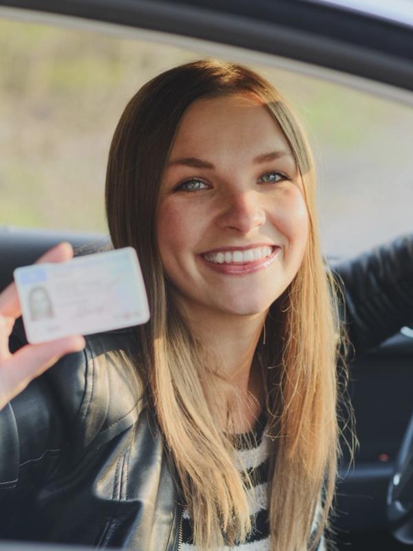 Smiling woman in a car holding up her driver's license.