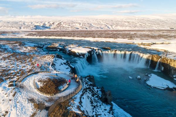 Amplia cascada que cae en aguas turquesa en un paisaje invernal nevado, con una plataforma de observación.