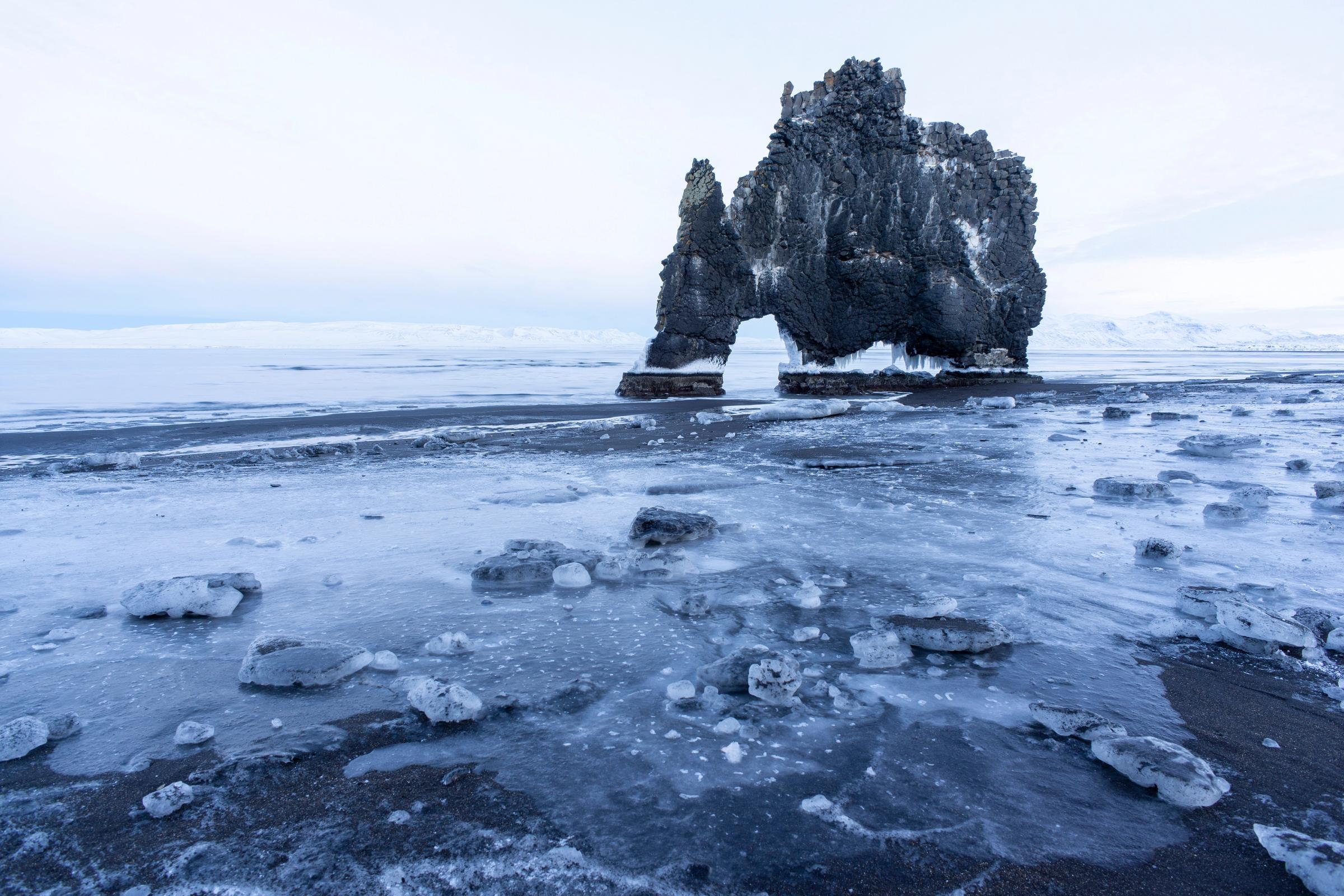 a large rock formation is sitting on top of a frozen beach .
