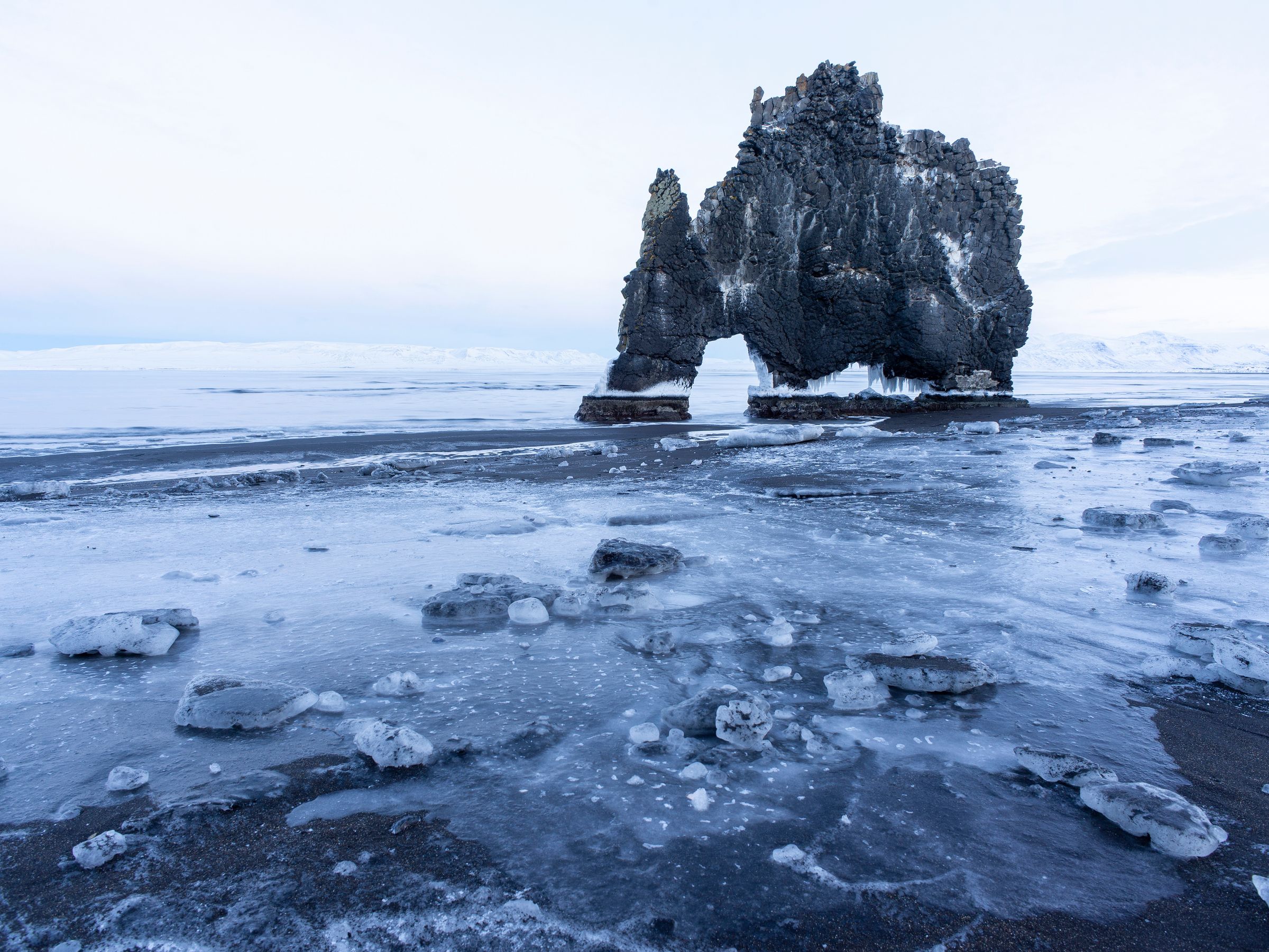 a large rock formation is sitting on top of a frozen beach .