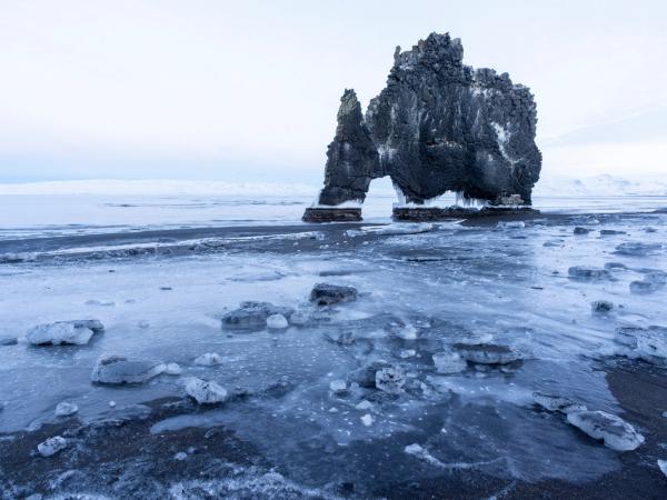 a large rock formation is sitting on top of a frozen beach .