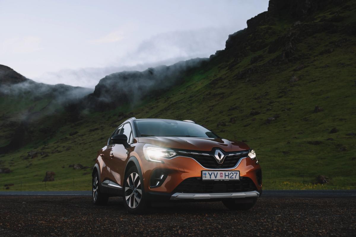 Renault Captur SUV rental Iceland parked on gravel with green hills and mist behind
