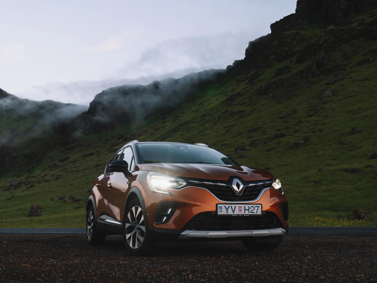 Vista frontal en tres cuartos del Renault Captur SUV Renault Captur de alquiler en Islandia, aparcado sobre grava con colinas verdes y niebla al fondo