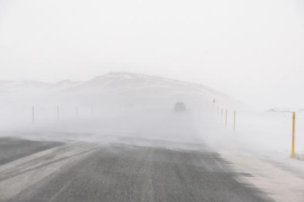 a car is driving down a snowy road in the snow blizzard in iceland.
