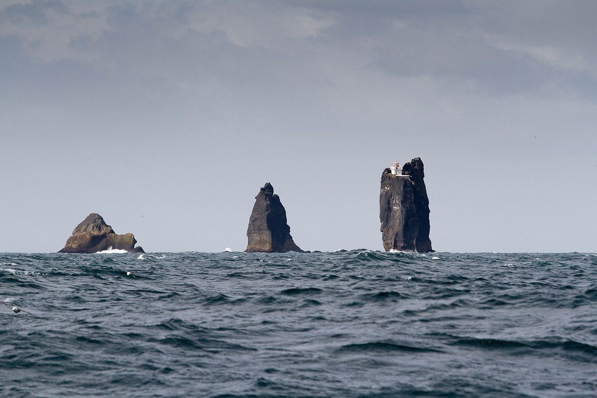 tres grande rocas en mitad del océano, una de ellas con un faro en la cima