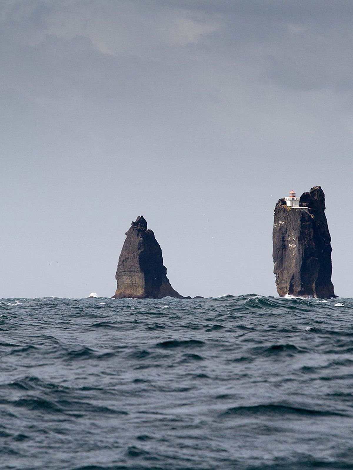 tres grande rocas en mitad del océano, una de ellas con un faro en la cima