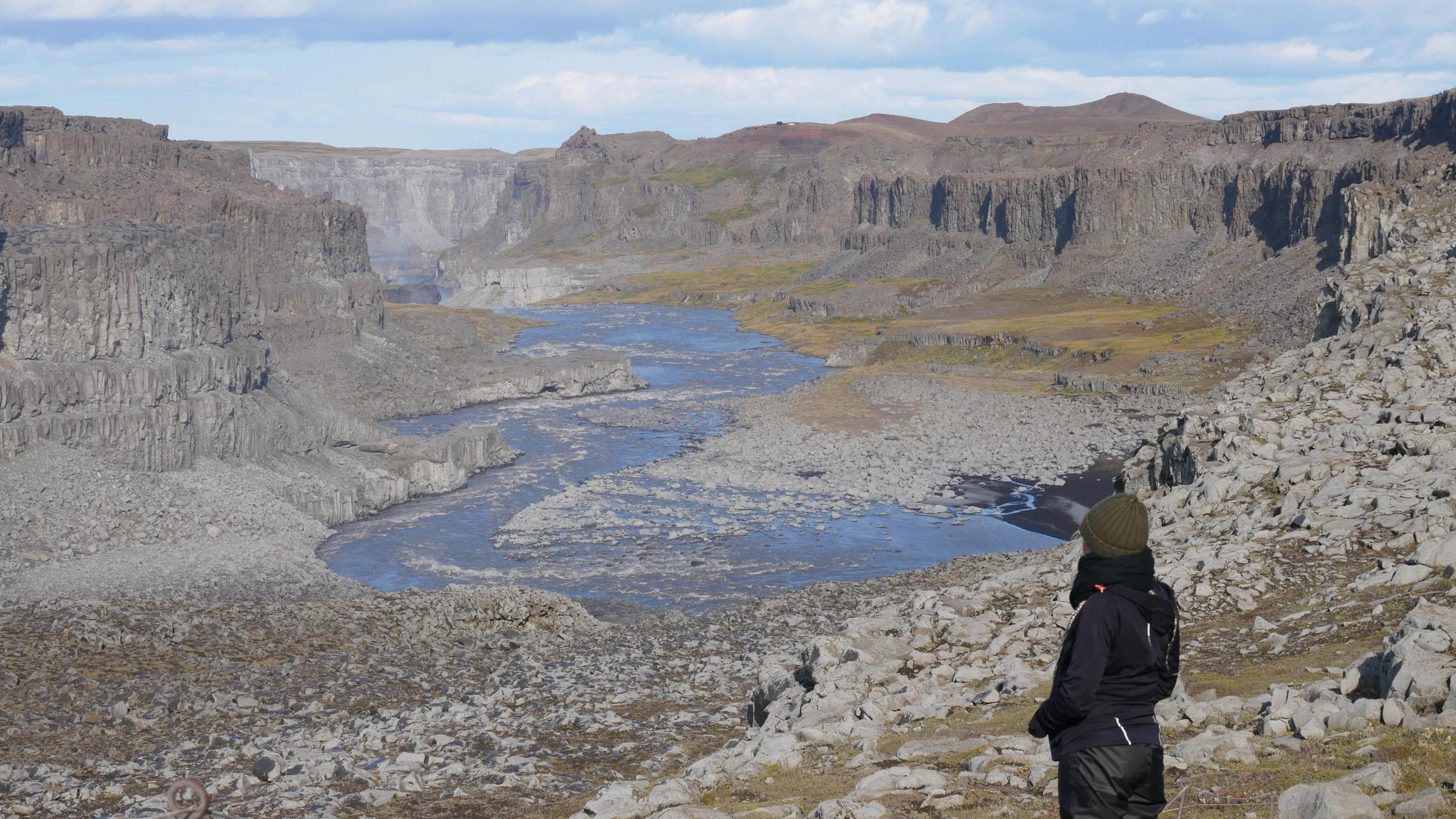 A person stands on a rocky overlook, gazing at a vast canyon with a winding river.