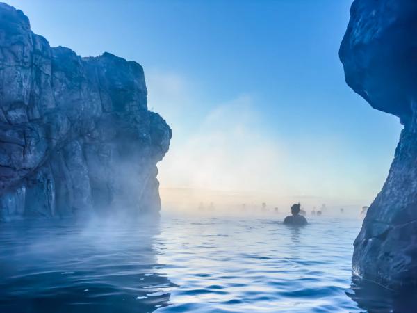 a person is swimming in a hot spring surrounded by rocks .