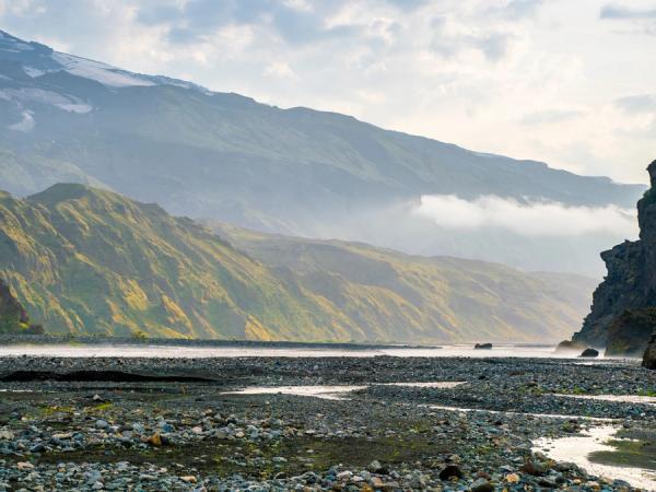 a river running through a rocky valley with mountains in the background .