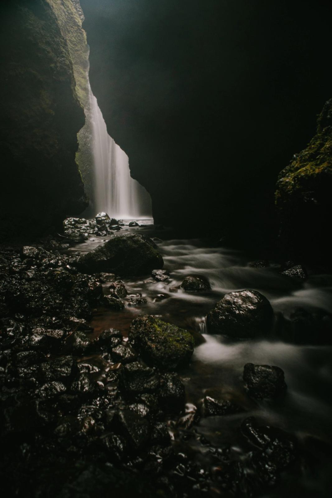 Cascada nebulosa dentro de una garganta rocosa y oscura con un arroyo difuminado fluyendo sobre las rocas.