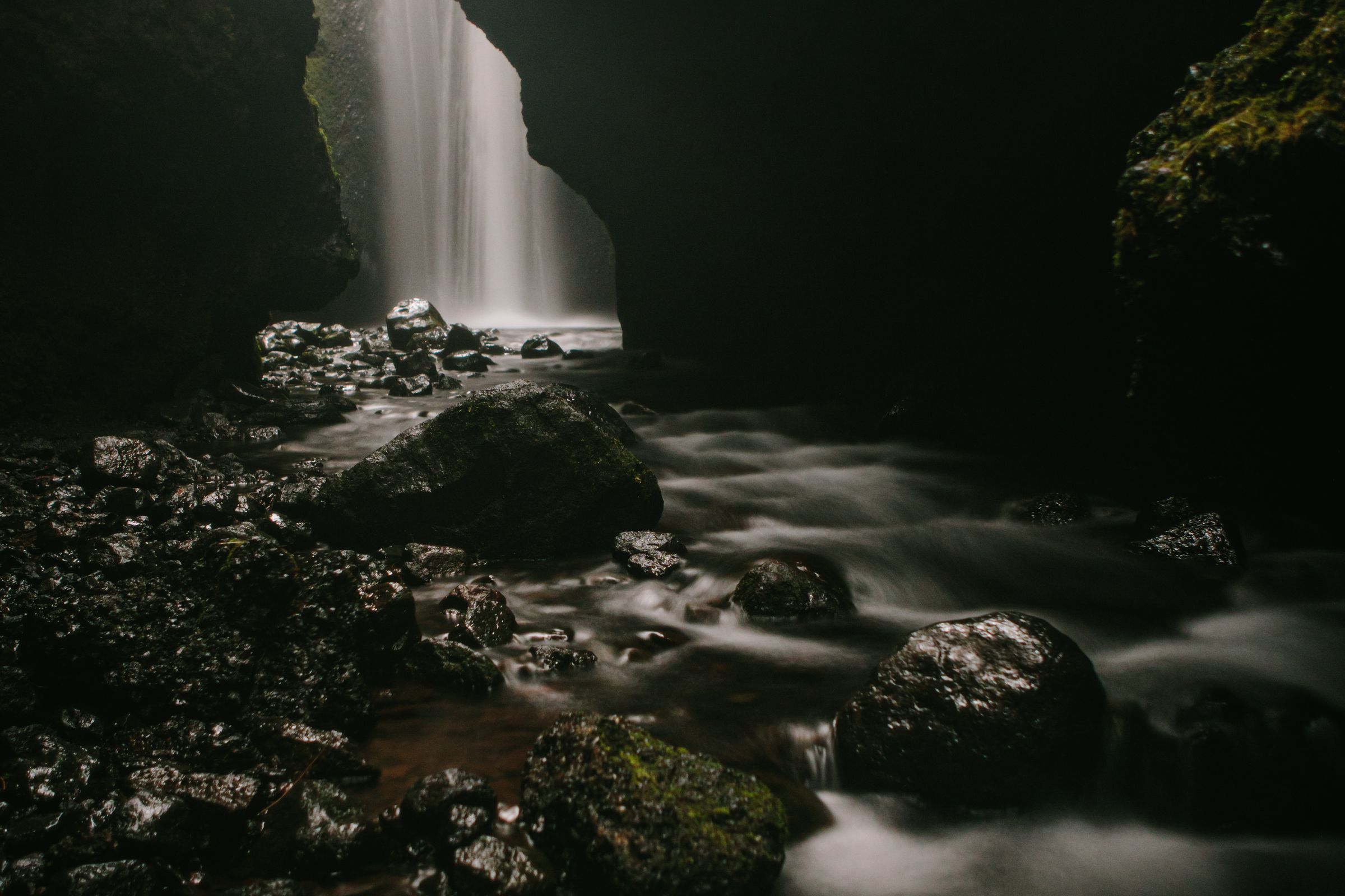 Cascada nebulosa dentro de una garganta rocosa y oscura con un arroyo difuminado fluyendo sobre las rocas.