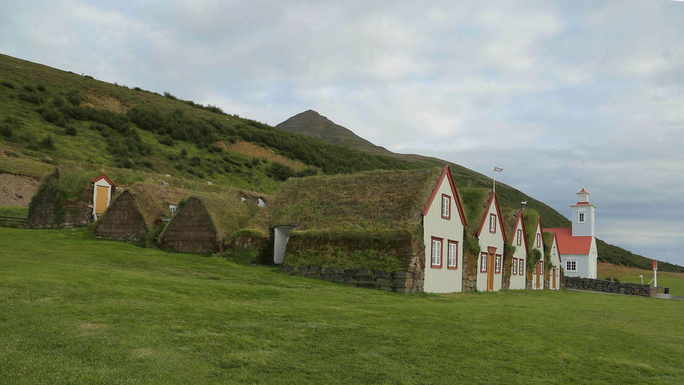 Casas tradicionales de turba y una iglesia blanca construida en una ladera verde.