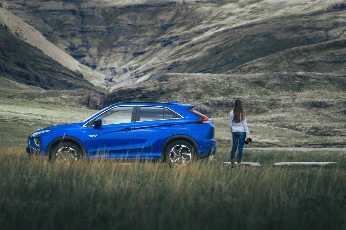 Vista lateral de un Mitsubishi Eclipse Cross aparcado sobre la hierba, con una persona de pie en un valle de montaña