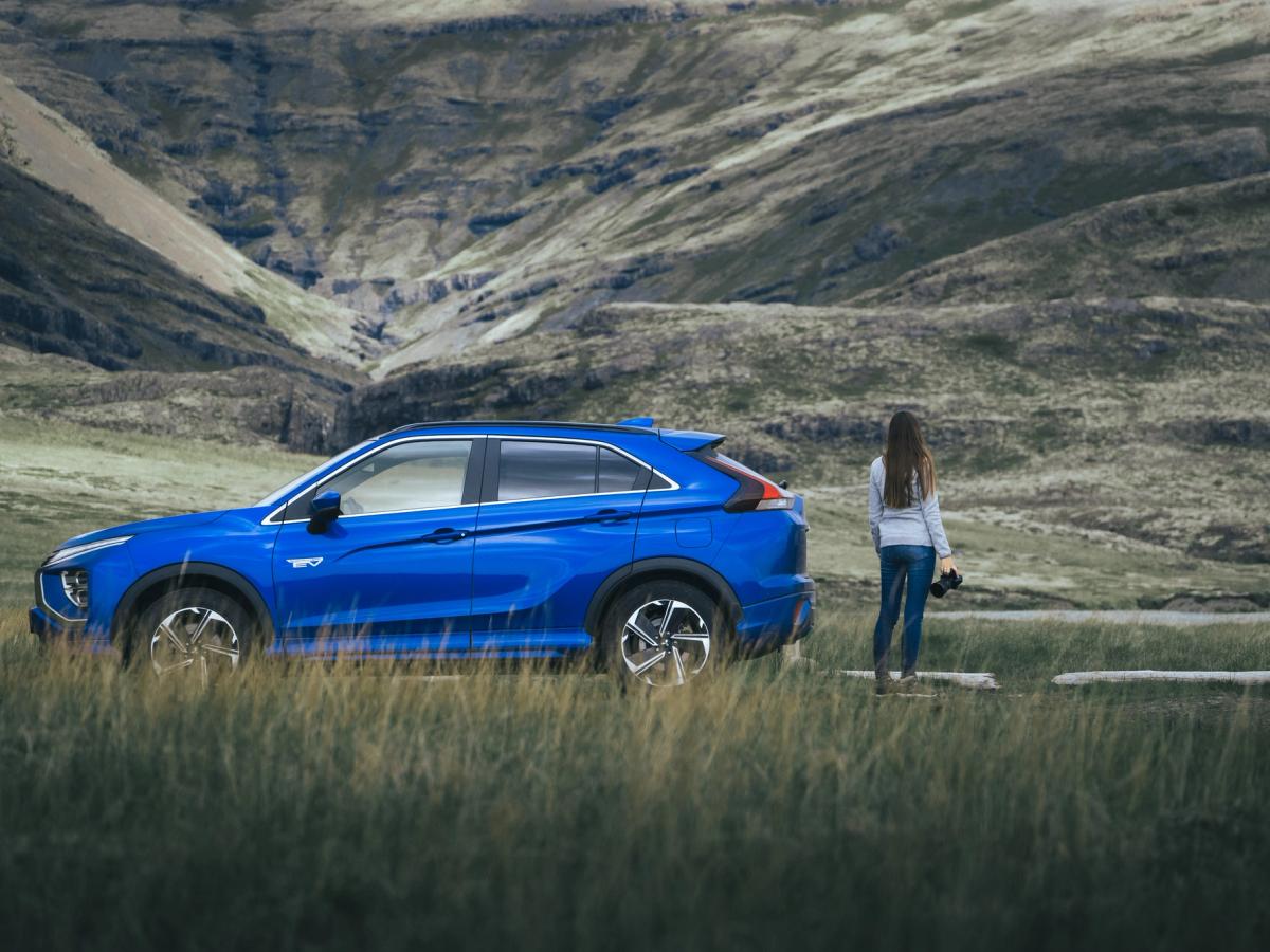 Mitsubishi Eclipse Cross Valley View Vista lateral de un Mitsubishi Eclipse Cross aparcado sobre la hierba, con una persona de pie en un valle de montaña