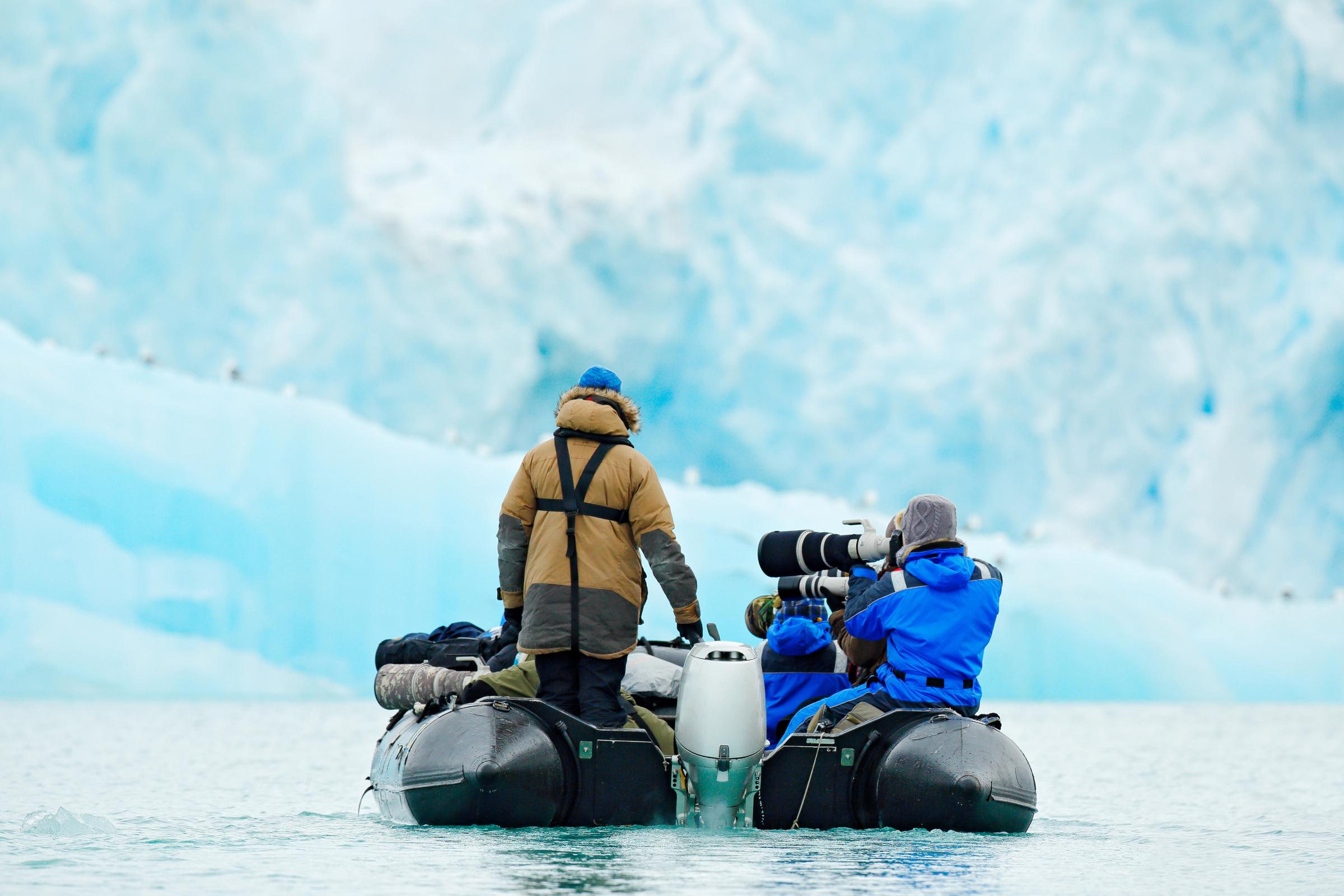 dos personas en una lancha haciendo fotos a un glaciar
