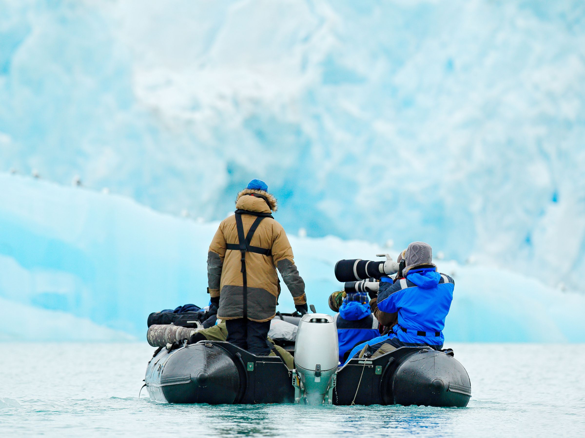 two people taking pictures of a glacier from a boat