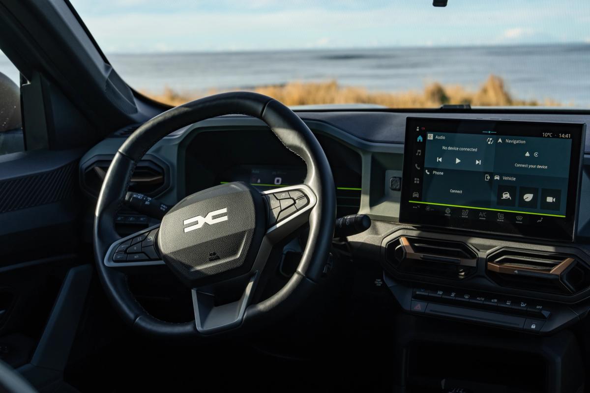 Painel de instrumentos de um Dacia Duster, com volante e ecrã tátil, virado para uma vista para o mar