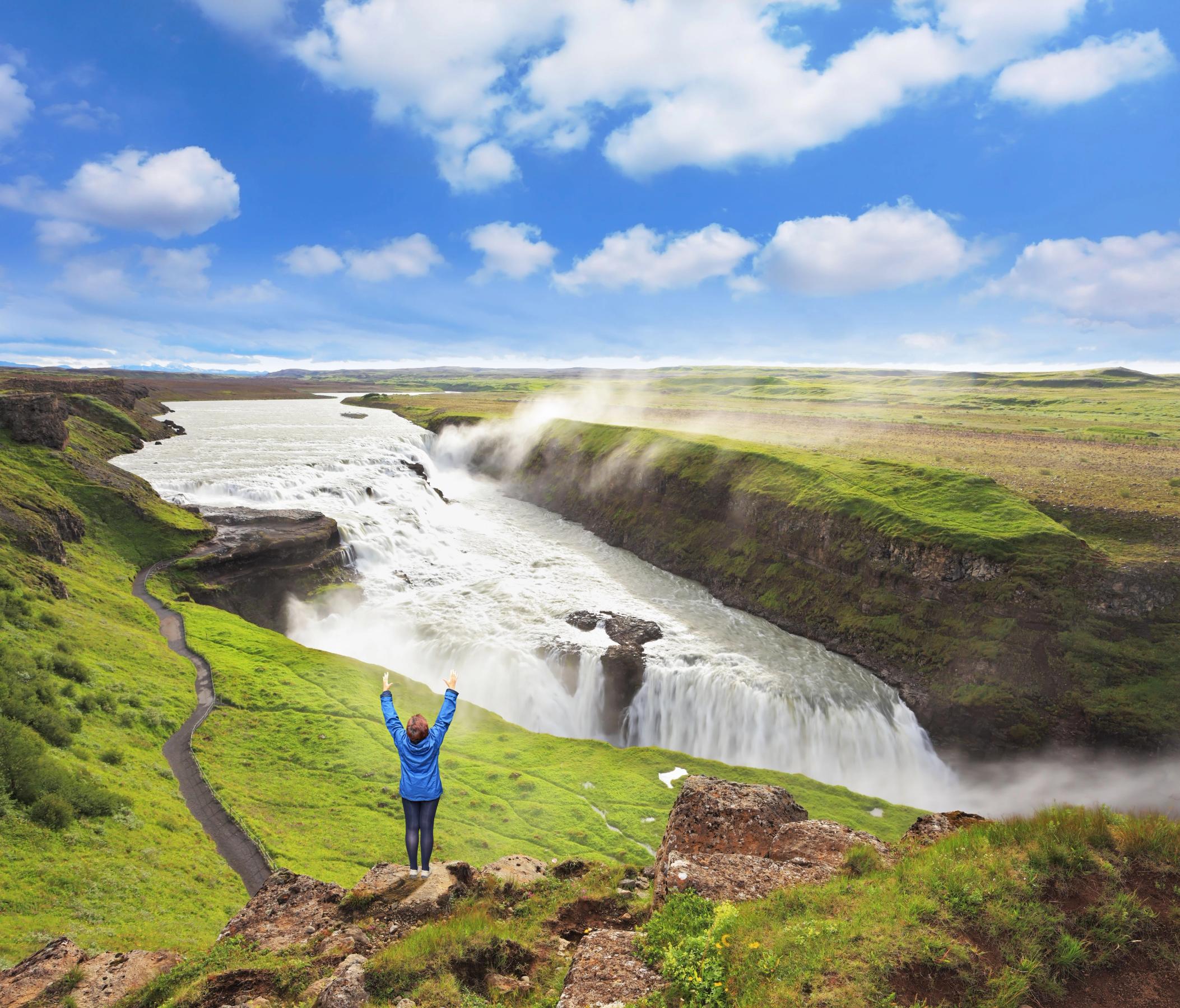 a woman is standing on top of a cliff overlooking a waterfall .