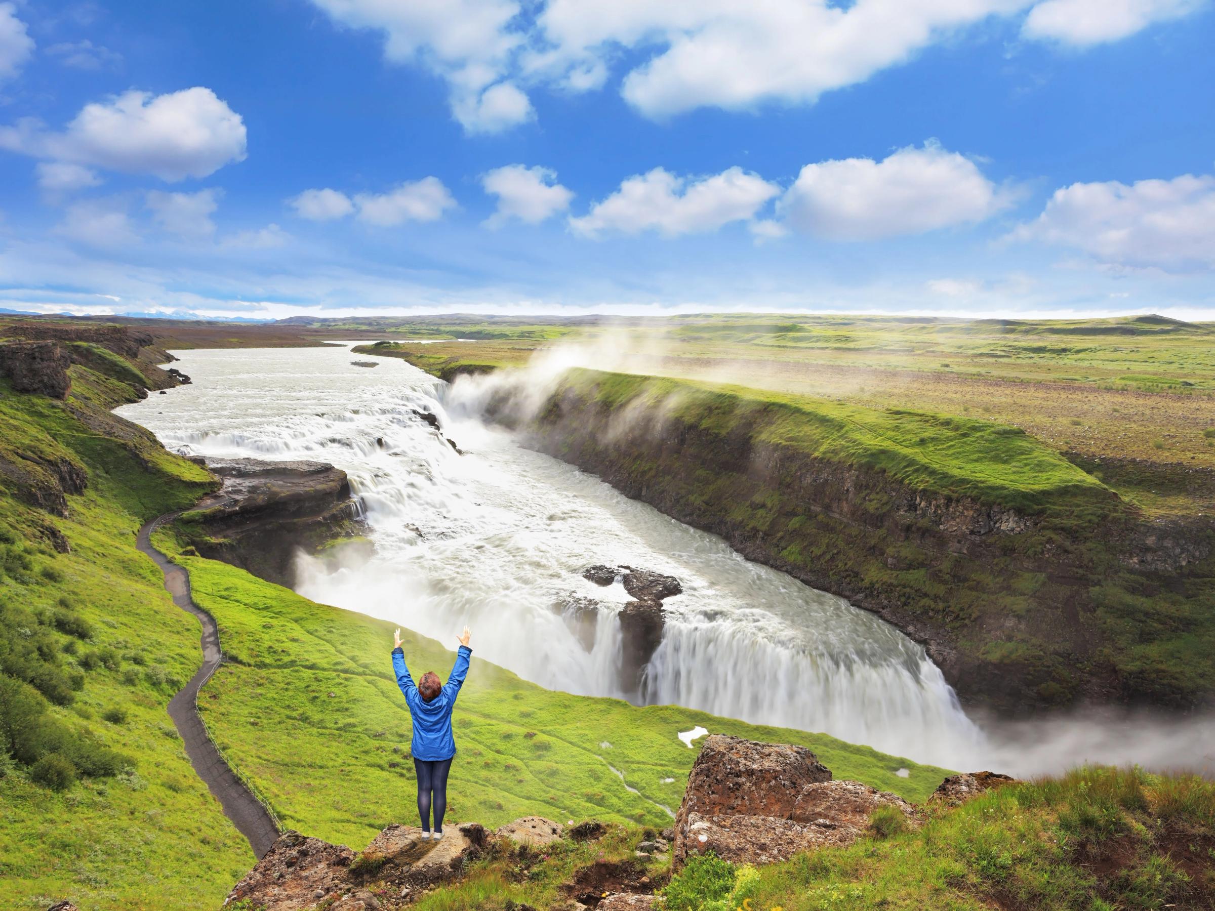 a woman is standing on top of a cliff overlooking a waterfall .