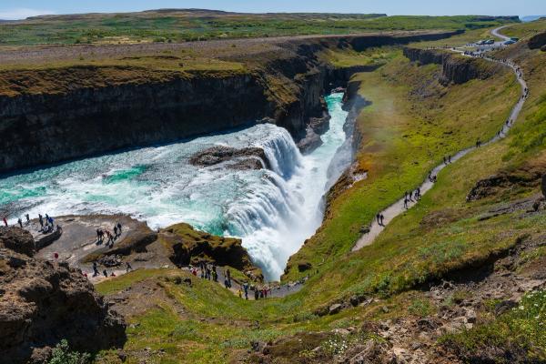 a group of people are walking down a path towards a waterfall .