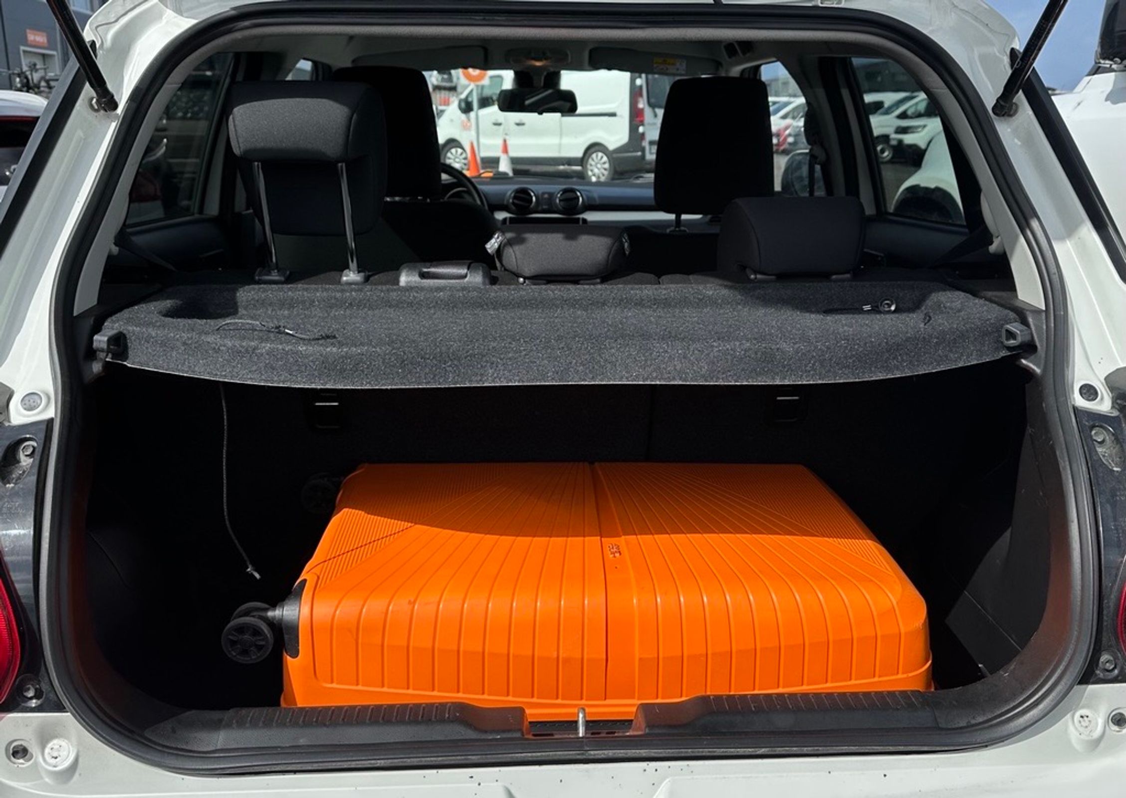A large orange suitcase in the open trunk of a white car.