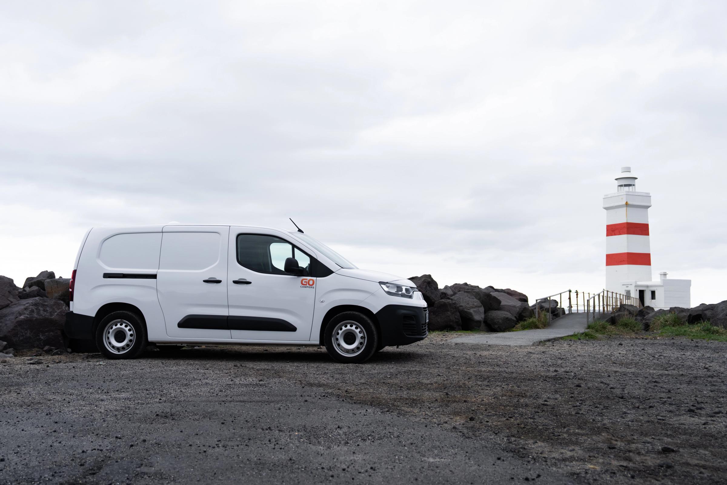 Seitenansicht eines kompakten Campervans, der in der Nähe eines gestreiften Leuchtturms geparkt ist, Island-Campervan