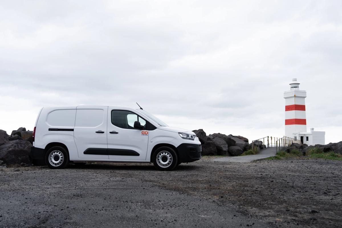 Seitenansicht eines kompakten Campervans, der in der Nähe eines gestreiften Leuchtturms geparkt ist, Island-Campervan