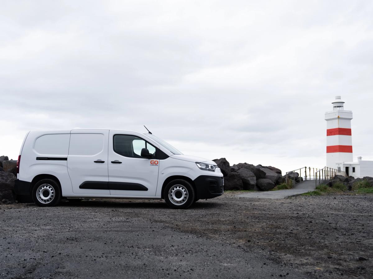 Kompakter Camper in Seitenansicht Seitenansicht eines kompakten Campervans, der in der Nähe eines gestreiften Leuchtturms geparkt ist, Island-Campervan