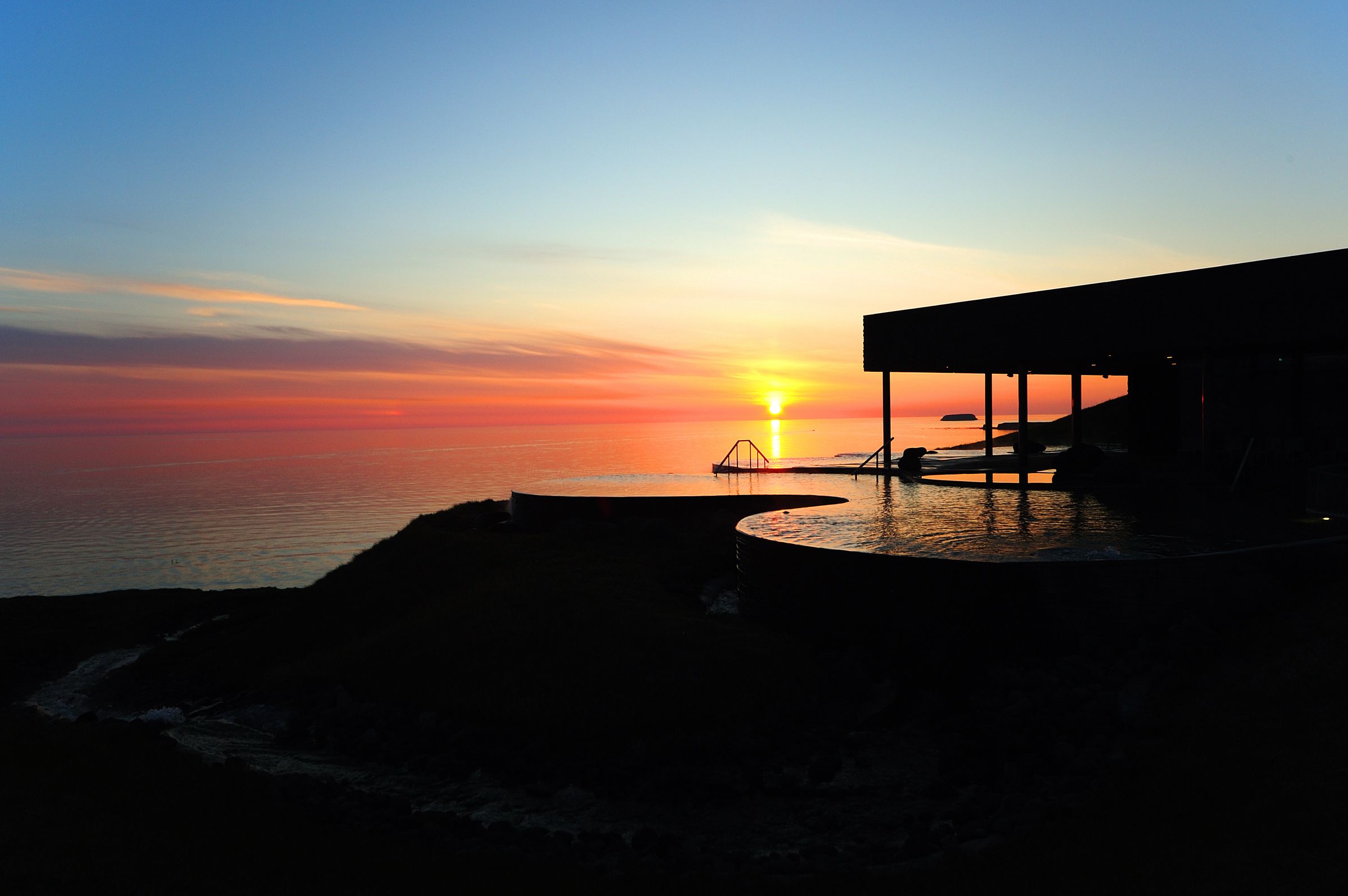 una puesta de sol sobre el océano con una piscina en primer plano.