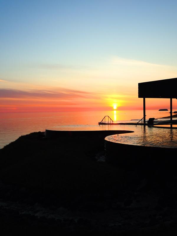 Vibrant sunset over the ocean, silhouetting a resort building and outdoor pools.