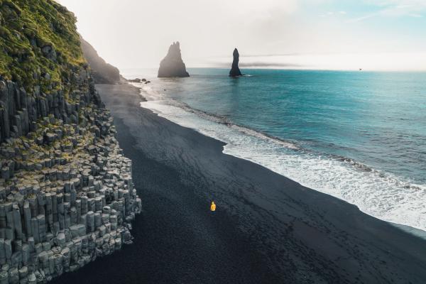 an aerial view of a person standing on a black sandy beach near the ocean .