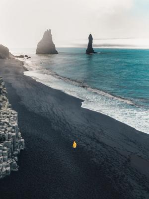 an aerial view of a person standing on a black sandy beach near the ocean .