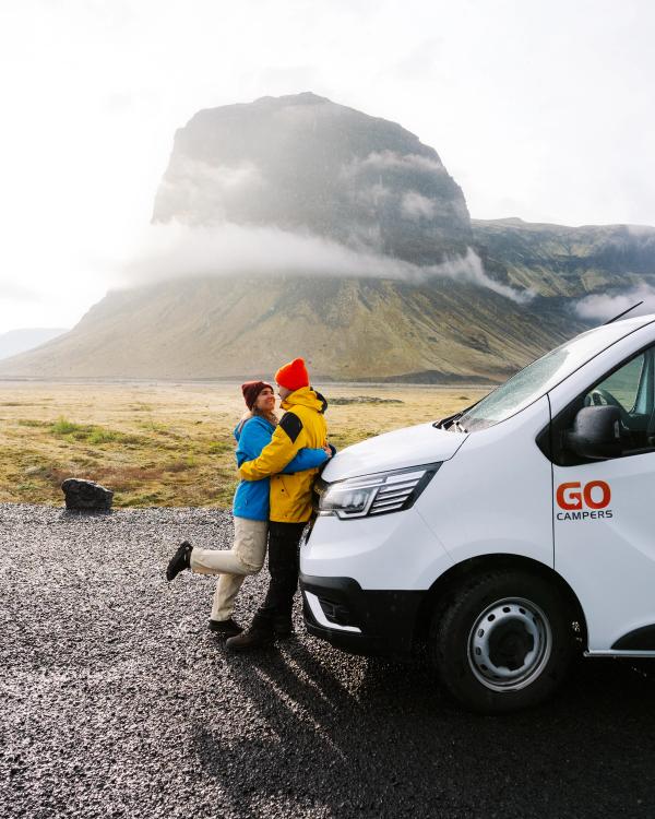 a man and woman hugging in front of a go camper van .