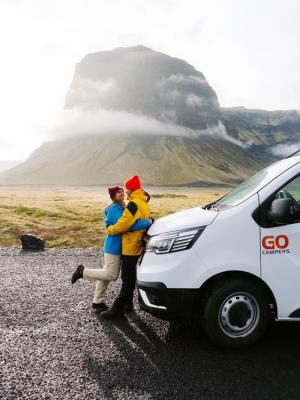 a man and woman hugging in front of a go camper van .