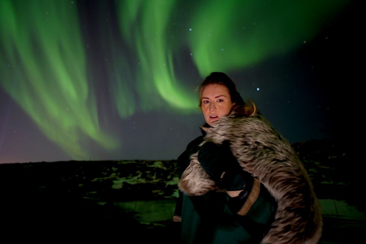 Una mujer sentada bajo la aurora boreal.