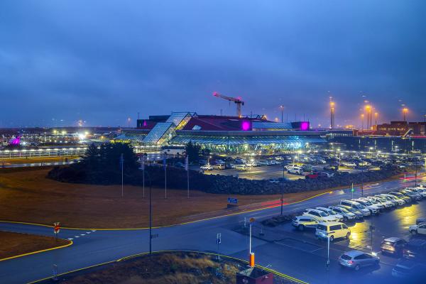 Modern airport terminal and parking lots brightly lit at night under a dark sky.